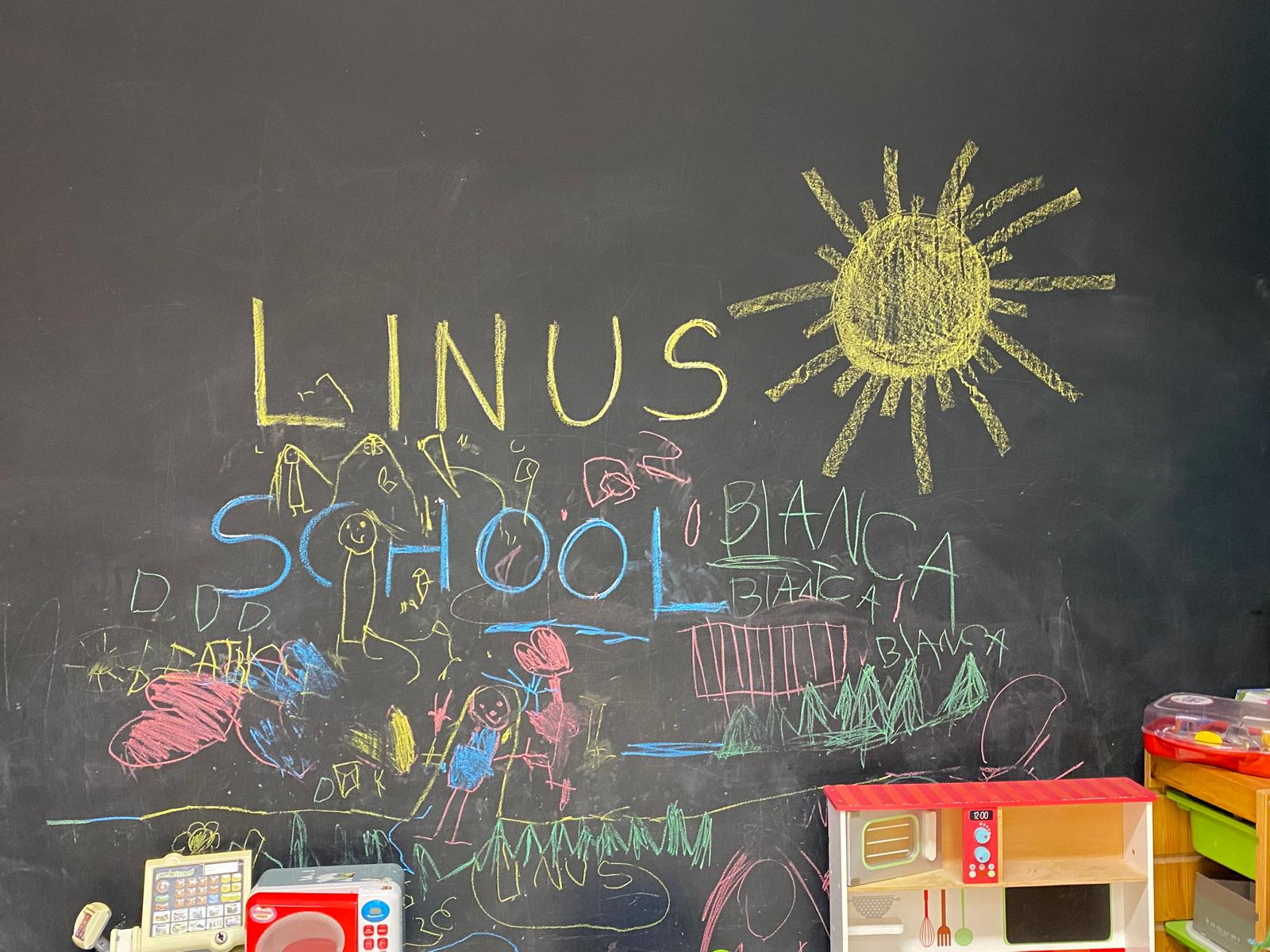 Lavagna con la scritta a gessetti «Linus School» e i disegni dei bambini